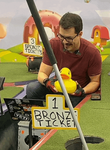 a man holds a yellow rubber duck in front of a 1 bronze ticket sign