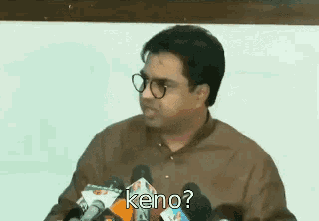 a man wearing glasses is standing in front of a microphone and talking to the media .