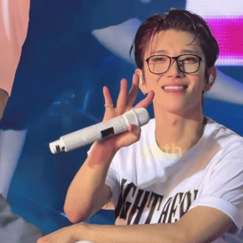 a man wearing glasses and a chicago shirt holds a microphone in his right hand