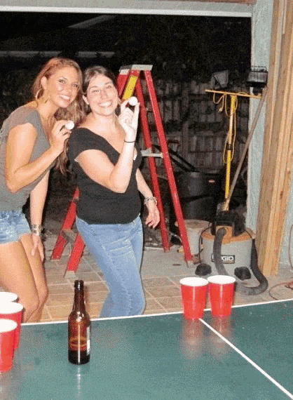 two women are playing ping pong with a bottle of beer on the table