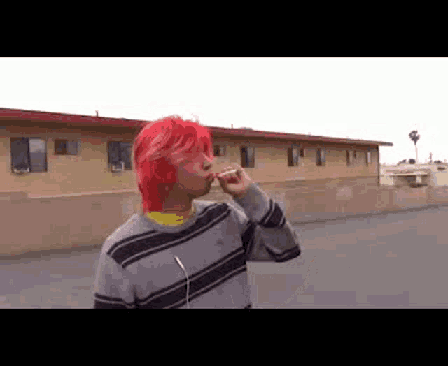 a young man with red hair is smoking a cigarette while wearing headphones .