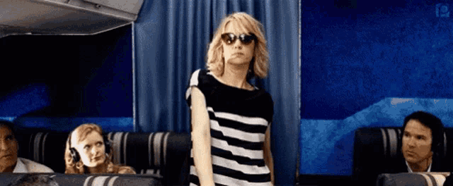 a woman wearing sunglasses and a striped shirt is standing on a plane