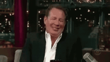 a man in a suit is sitting in front of a microphone and laughing .