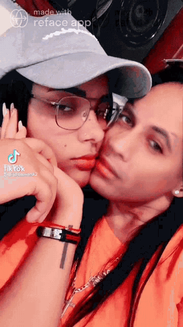 a woman wearing glasses and a hat is kissing another woman 's cheek