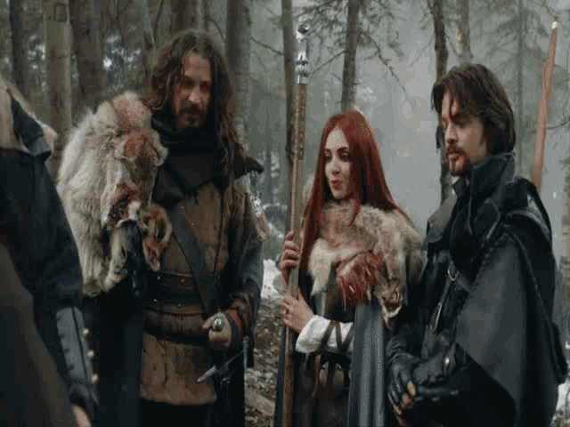 a group of medieval people are standing in the woods .