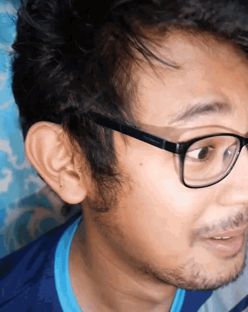 a man wearing glasses and a blue shirt looks to his right