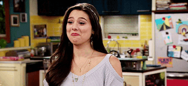a woman is making a funny face in a kitchen while wearing a sweater .