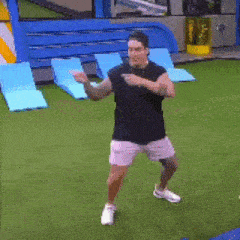 a man in a black shirt and pink shorts is dancing on a lawn with the words chaca chaca por delante written below him
