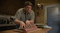 a man is cutting a large piece of meat on a cutting board in a kitchen
