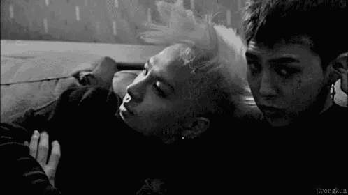 a black and white photo of two men laying on a couch . one of the men has a tattoo on his forehead .