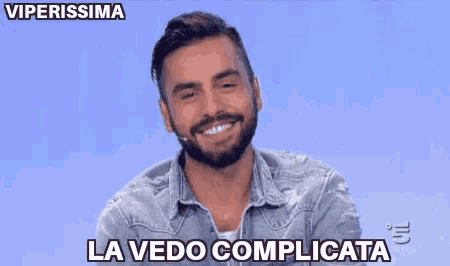 a man with a beard is sitting in front of a blue background and says la vedo complicatata