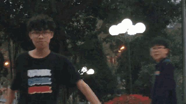 a person wearing glasses and a black shirt smiles in front of trees