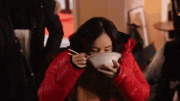 a woman in a red jacket is eating noodles with chopsticks .