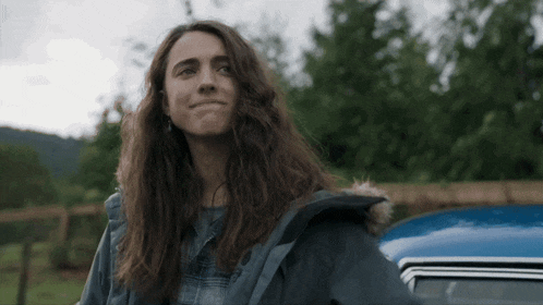 a woman with long hair is standing in front of a car