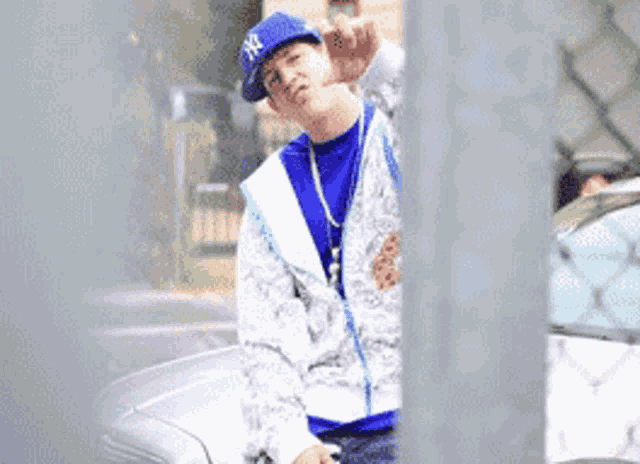 a man wearing a ny hat is standing next to a white car