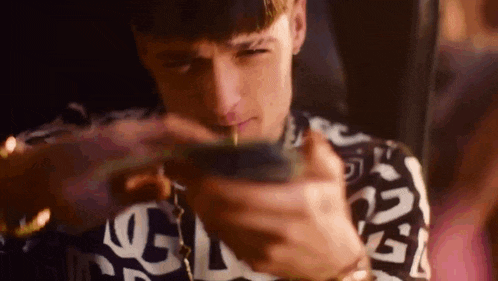 a young man is smoking a cigarette while holding a stack of money in his hand .