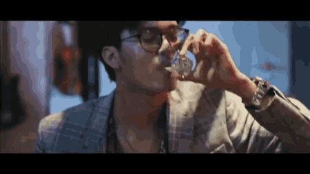 a man in a suit and glasses drinking from a glass