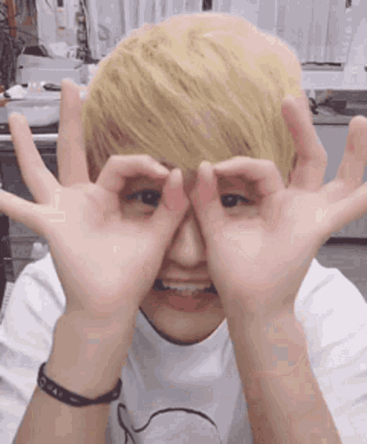 a young man with blonde hair making a funny face with his hands