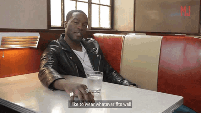 a man in a leather jacket sits at a diner table with a glass of water