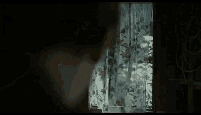 a person is looking out a window with a floral curtain .