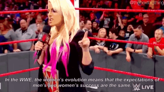 a woman is standing in a wrestling ring holding a microphone and pointing at the crowd .