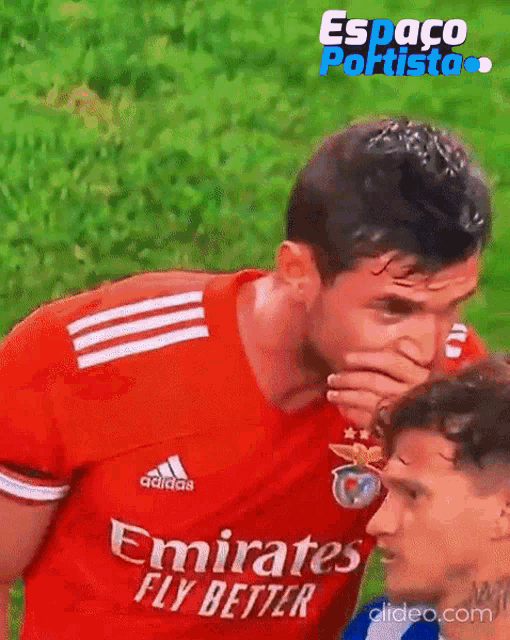 a soccer player wearing a red emirates fly better jersey covering his mouth