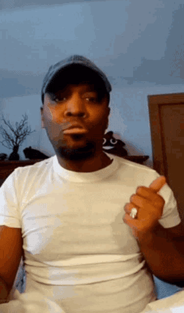 a man wearing a hat and a white shirt is giving a thumbs up sign