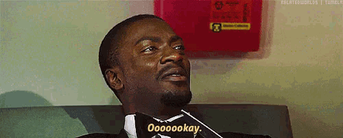 a man in a suit and bow tie is sitting on a couch and says oooooookay .