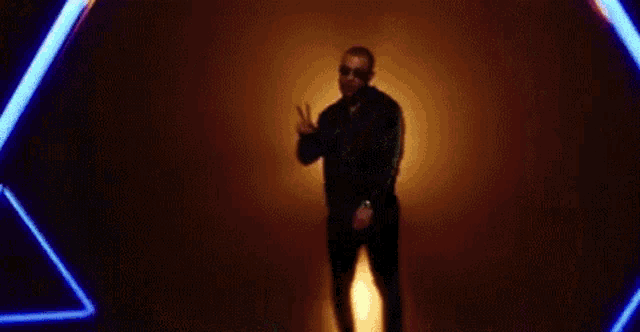a man in sunglasses is standing in a dark room with neon lights .