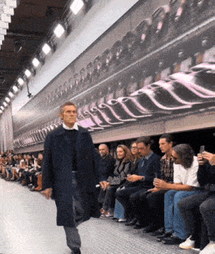 a man is walking down a runway in front of a wall with a picture of a machine on it
