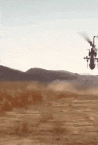 a helicopter is flying over a deserted area with mountains in the background