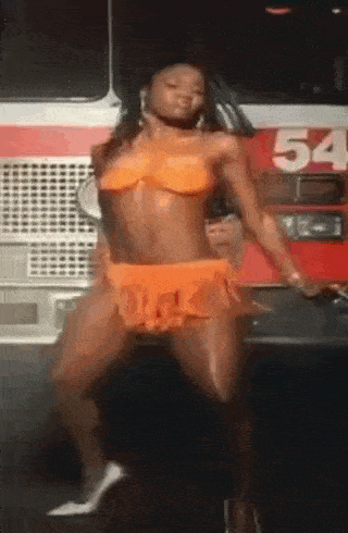a woman in an orange bikini is dancing in front of a red fire truck with the number 54 on it .