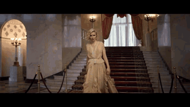 a woman in a long gold dress is walking down a red carpeted staircase