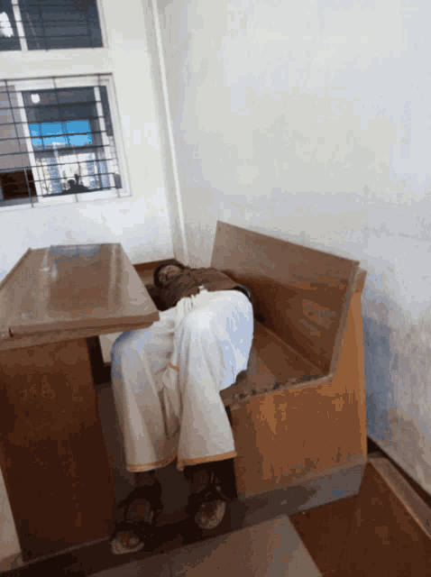 a man is sleeping on a wooden bench in a room