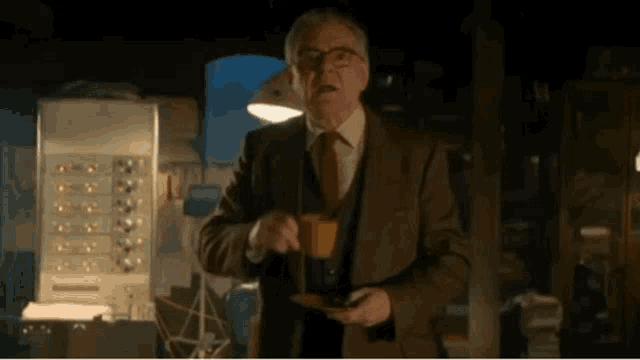 a man in a suit and tie is standing in a dark room holding a cup of coffee .