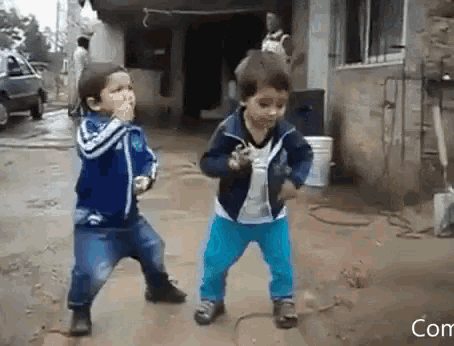 two young boys are dancing in front of a building with the word com below them
