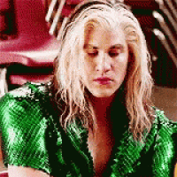a woman with blonde hair and a green jacket is sitting in a chair .