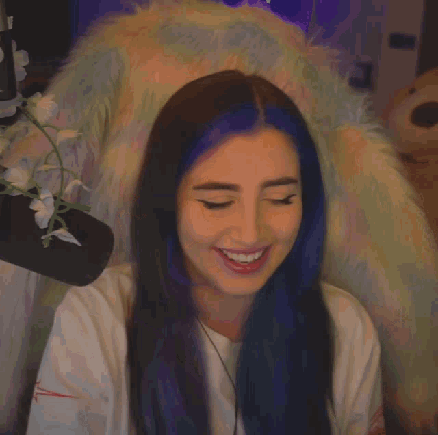 a woman with blue hair is sitting in a chair with a flower in the background