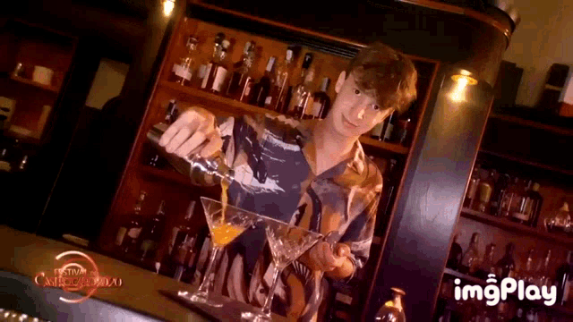 a man is pouring a drink into a martini glass in a bar .