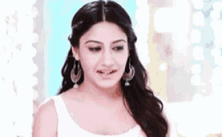 a woman wearing earrings and a white tank top is making a funny face .