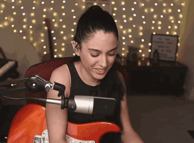 a woman is singing into a microphone while playing an orange guitar