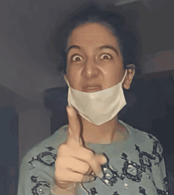 a woman wearing a face mask is making a funny face and pointing at the camera