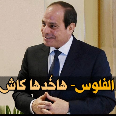 a man in a suit and tie stands in front of a sign with arabic writing on it