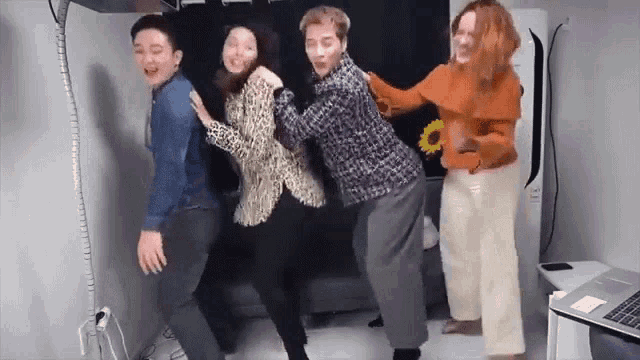 a group of people are dancing together in a room with a laptop on the floor .