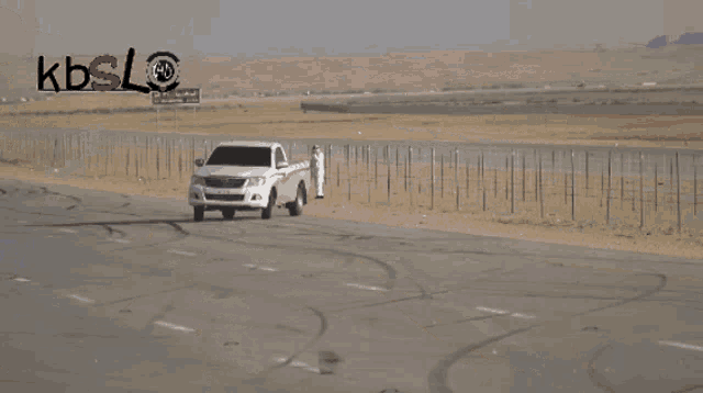 a white truck driving down a highway with kbsl written on the bottom
