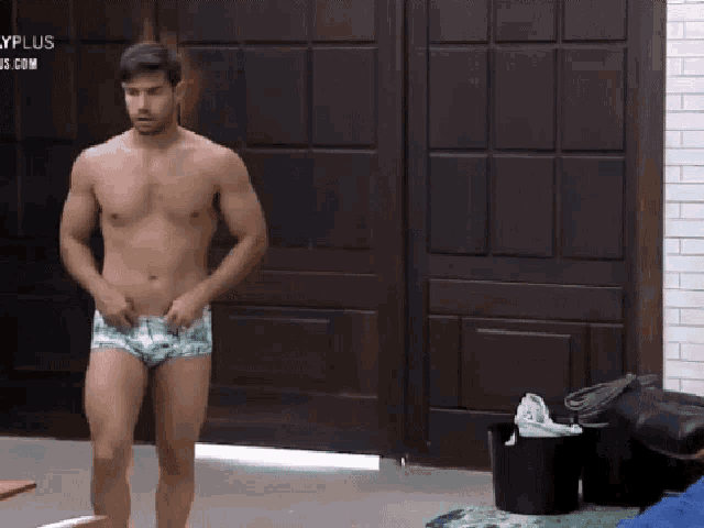 a shirtless man in underwear is standing in front of a wooden door