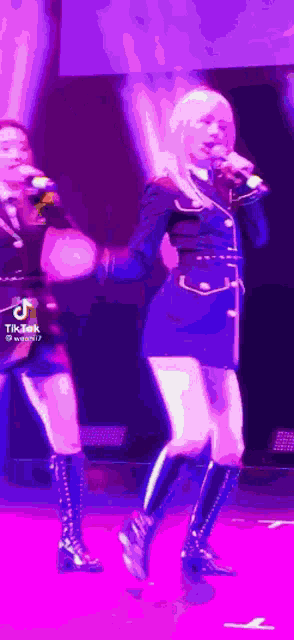two women are singing into microphones on a stage in a dark room .