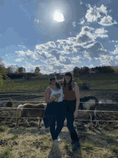 two women are posing for a picture in a field with horses in the background