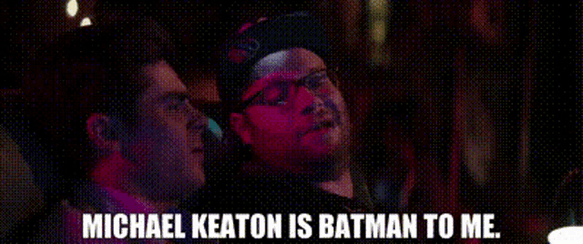two men are sitting next to each other and one of them is talking about michael keaton being batman to me .