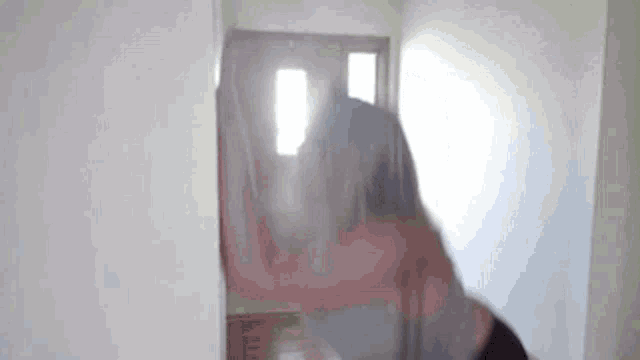 a woman is standing in a hallway in front of a door and looking at herself in a mirror .